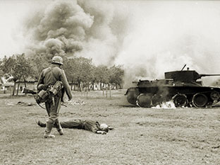 Немецкий солдат и труп советского солдата у горящего танка БТ-7 в 1941 году